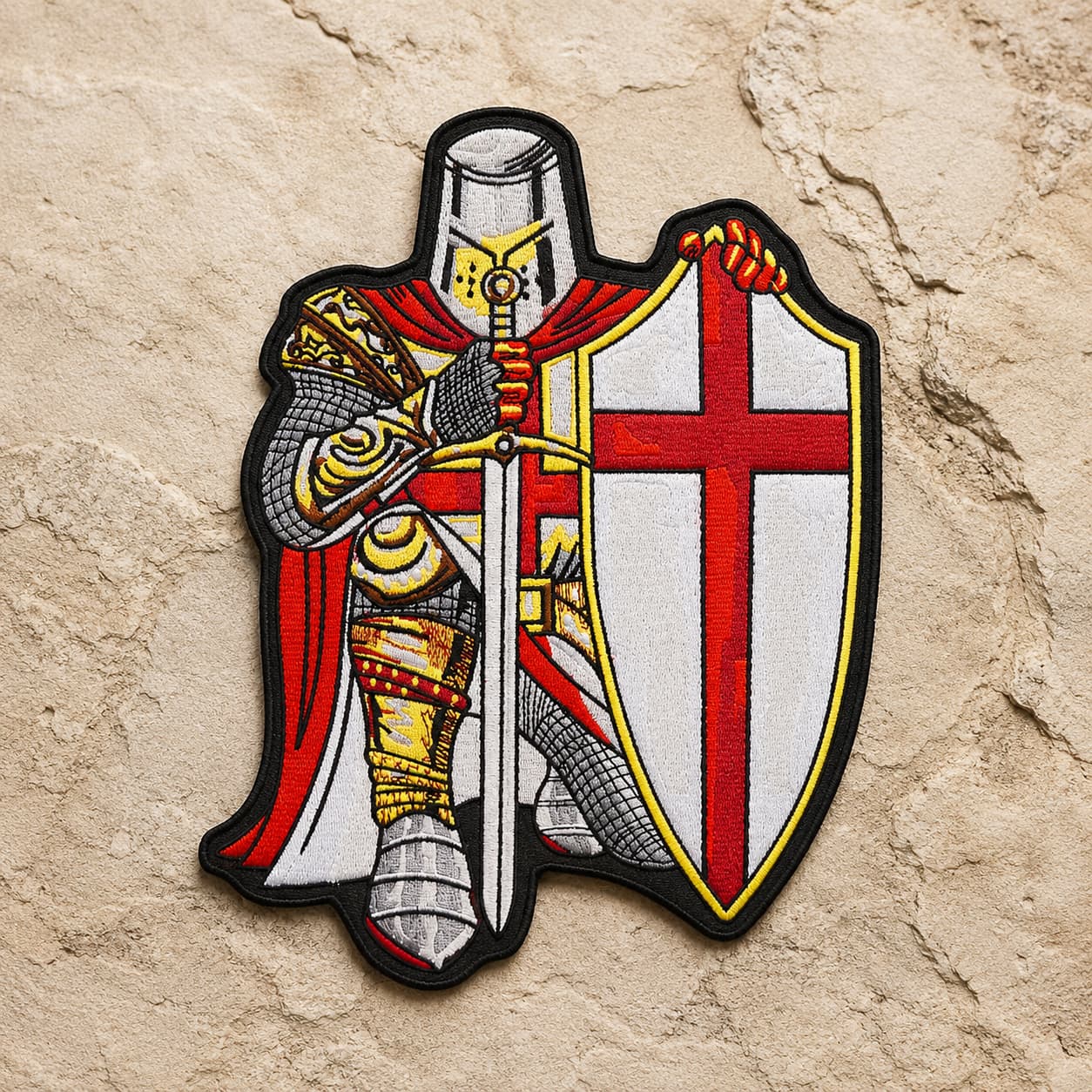 Patch Écusson prière du Templier en tissu brodé posé sur une pierre claire médiévale.