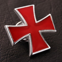 Gros plan du Pin’s Croix du Temple en alliage métallique rouge et argenté sur fond sombre.