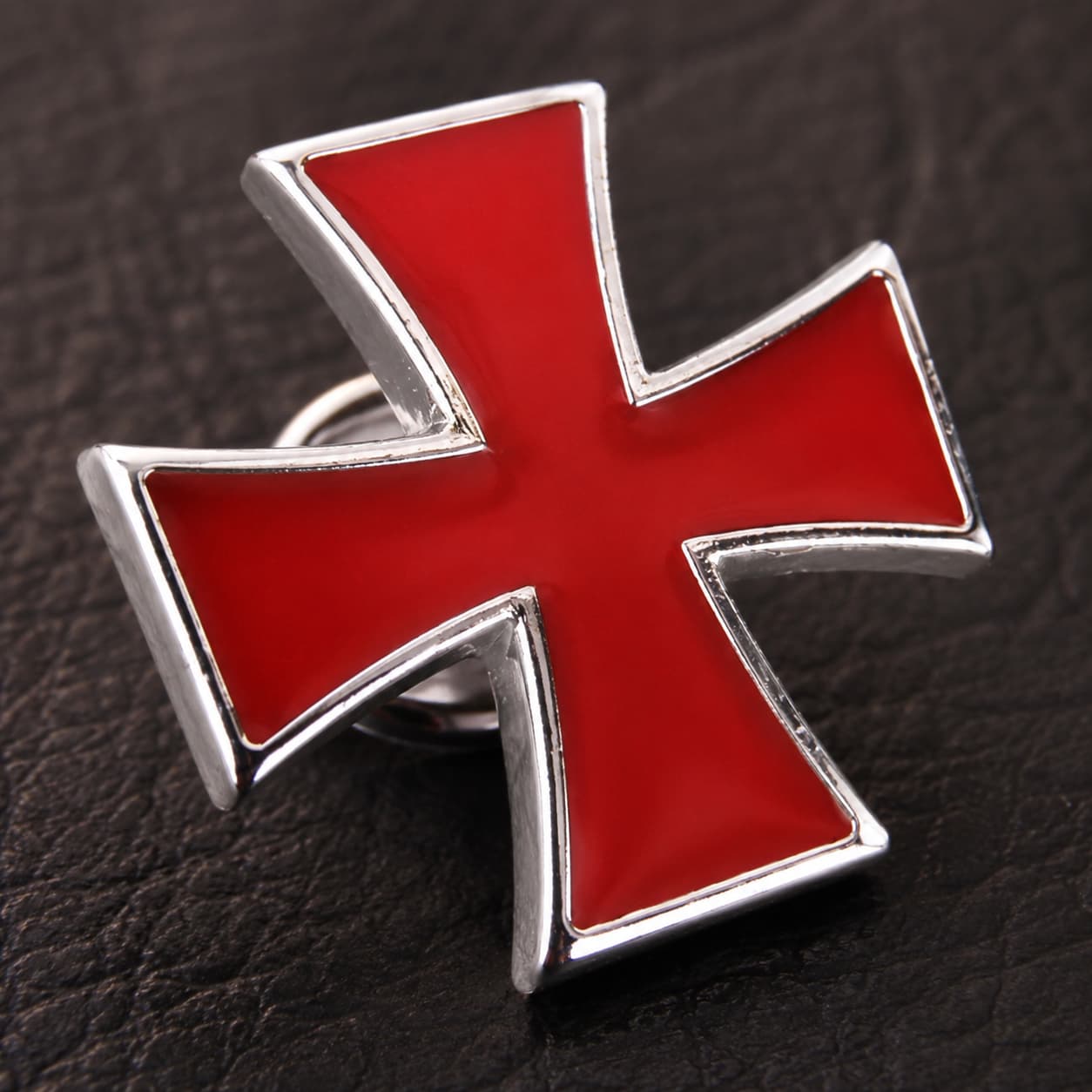 Gros plan du Pin’s Croix du Temple en alliage métallique rouge et argenté sur fond sombre.
