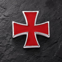 Pin’s Croix du Temple en alliage métallique rouge et argenté sur fond de pierre médiévale sombre.