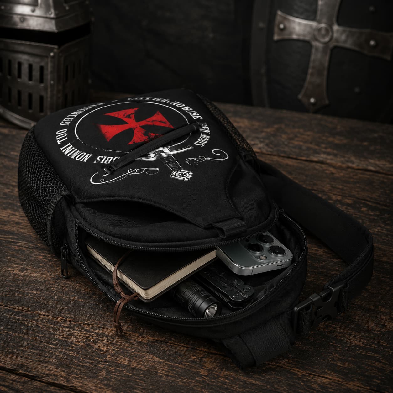 Sac à bandoulière Non Nobis en polyester ouvert sur bois ancien avec téléphone, carnet et accessoires rangés à l’intérieur.