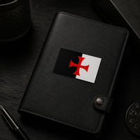 Sticker Bannière du Temple en vinyle appliqué sur un carnet en cuir noir dans une ambiance sombre.