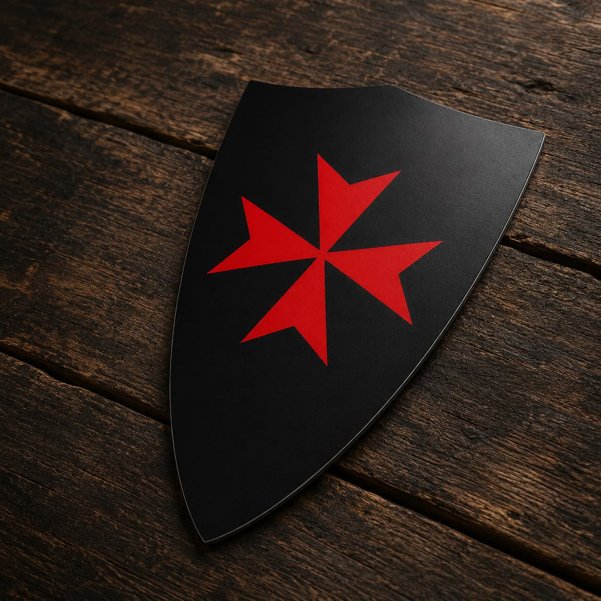 Sticker Bouclier Templier en vinyle adhésif vu de trois quarts sur bois ancien, montrant la forme du bouclier noir et sa croix rouge.