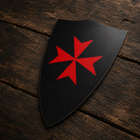 Sticker Bouclier Templier en vinyle adhésif vu de trois quarts sur bois ancien, montrant la forme du bouclier noir et sa croix rouge.
