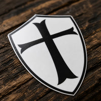 Sticker du Chevalier Templier en vinyle résistant posé sur bois ancien sombre, avec croix noire et contour du bouclier visibles.