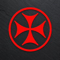 Sticker Croix de Malte en vinyle rouge sur fond ardoise sombre.